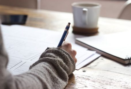 Background Check - person writing on brown wooden table near white ceramic mug