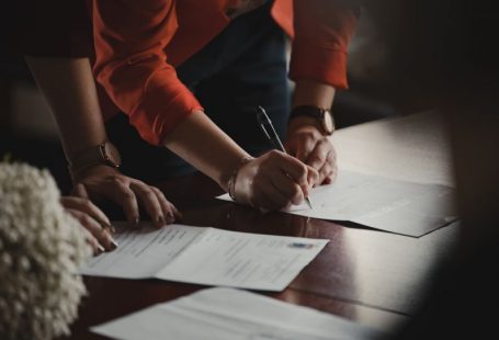 Contract Signing - person in orange long sleeve shirt writing on white paper