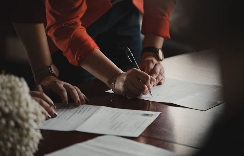 Contract Signing - person in orange long sleeve shirt writing on white paper
